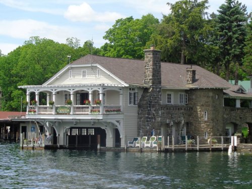 A charming lakeside house with a stone chimney, surrounded by greenery and featuring a porch with flower boxes.