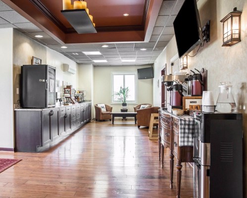 A cozy lobby area with a coffee station, seating, and large windows, featuring wooden floors and warm lighting.