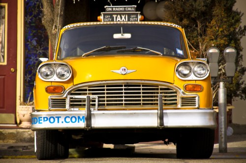 A classic yellow taxi cab parked on a street, with a "On Radio Call" sign on top and a website on the side.