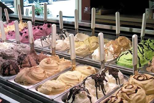 A colorful display of various gelato flavors in metal containers, each topped with a scoop and a serving spoon.