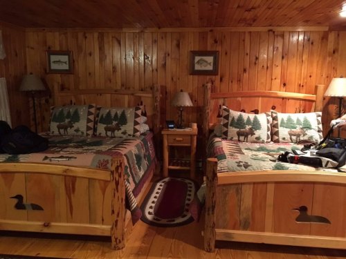 Cozy cabin bedroom with two wooden beds, rustic decor, and nature-themed bedding against a wooden wall.