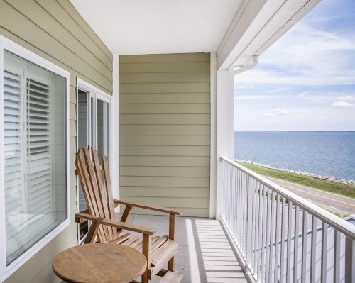 A wooden chair and small table on a balcony overlooking a calm sea under a clear sky.