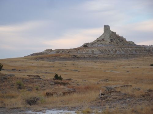 A rocky outcrop rises above a grassy plain under a cloudy sky, showcasing a rugged, natural landscape.