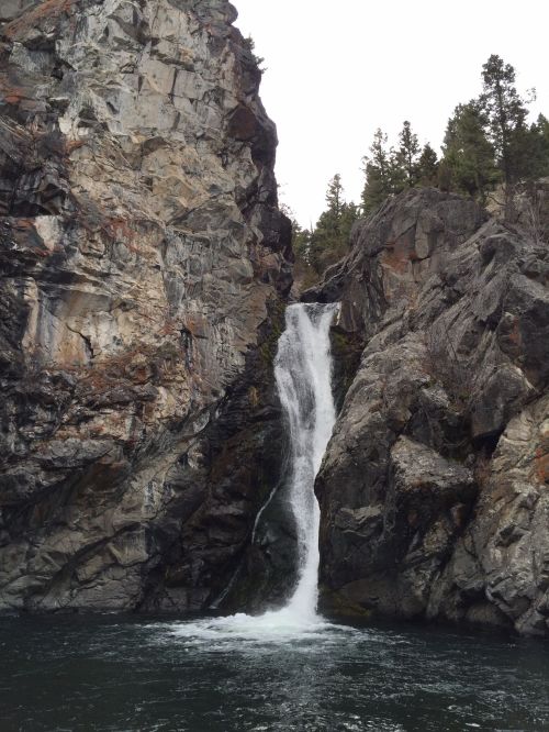 A waterfall cascading down rocky cliffs into a serene body of water, surrounded by trees and rugged terrain.