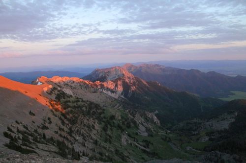 Sunset over rugged mountains, casting warm light on peaks and valleys under a colorful sky.