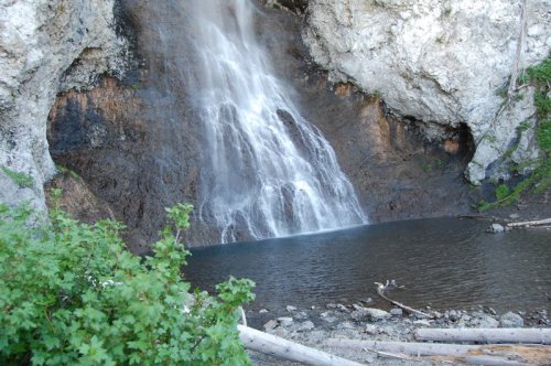 A serene waterfall cascading down rocky cliffs into a calm pool, surrounded by greenery and natural rock formations.