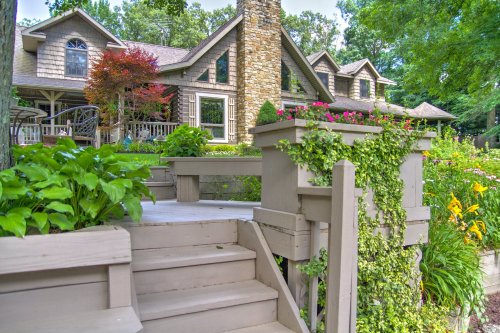 A beautiful home surrounded by lush greenery and colorful flowers, featuring a stone chimney and a welcoming porch.