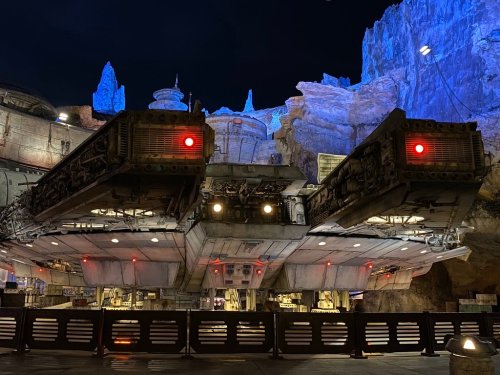 A detailed view of a futuristic spaceship in a themed setting, illuminated by blue and red lights at night.
