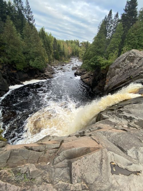 A scenic view of a waterfall cascading into a river, surrounded by lush green trees and rocky terrain.