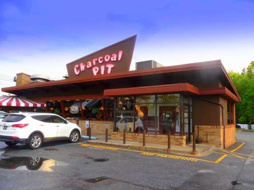 Exterior of Charcoal Pit restaurant with a modern design, featuring a sign and parked cars in the lot.