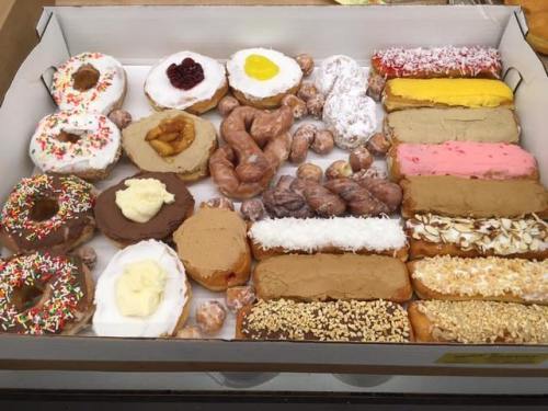 A variety of colorful donuts and pastries arranged in a box, featuring sprinkles, frosting, and different toppings.
