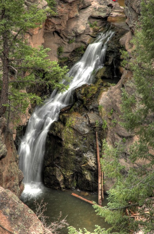 A serene waterfall cascades over rocky cliffs, surrounded by lush green trees and a tranquil pool below.