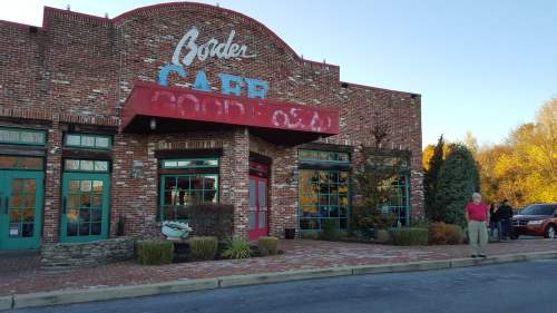A brick building with colorful windows and a sign reading "Café" in a scenic outdoor setting. People are gathered outside.