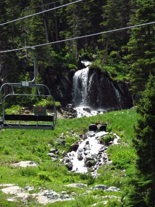 A ski lift overlooks a lush green landscape with a waterfall and stream flowing through rocky terrain.