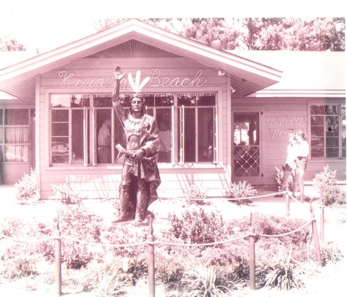 A vintage photo of a statue in front of a building labeled "Keenan's Beach," surrounded by greenery.