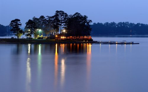 A serene lake at dusk, with a small island featuring a lit building and reflections on the water.