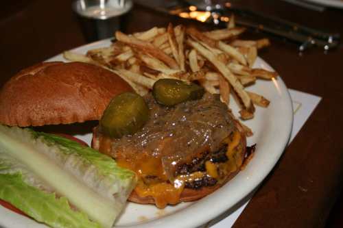 A juicy cheeseburger with pickles, lettuce, and a side of crispy French fries on a plate.