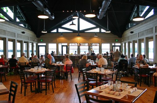 A spacious restaurant interior with wooden tables, chairs, and large windows overlooking a scenic view.