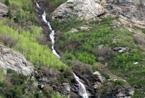 A cascading waterfall flows down rocky terrain, surrounded by lush green vegetation and rugged cliffs.
