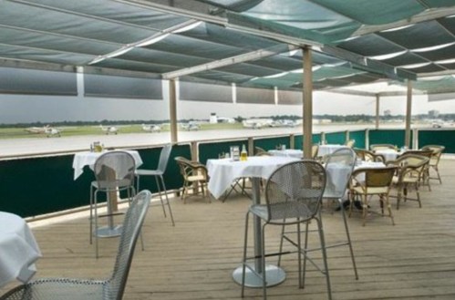 Outdoor dining area with tables and chairs overlooking an airport runway.