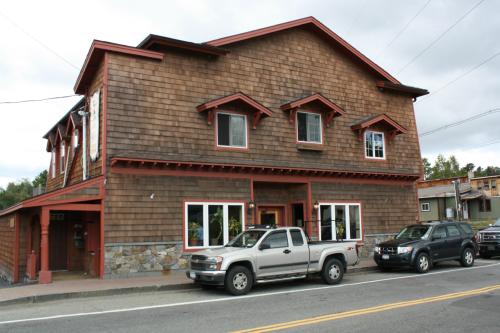 A two-story wooden building with a sloped roof, featuring multiple windows and parked cars in front.
