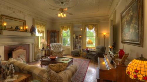 Cozy living room with vintage decor, large windows, a piano, and warm lighting. Elegant furnishings and a welcoming atmosphere.