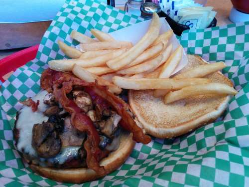 A burger with mushrooms, cheese, and bacon, served with a side of golden French fries in a red basket.