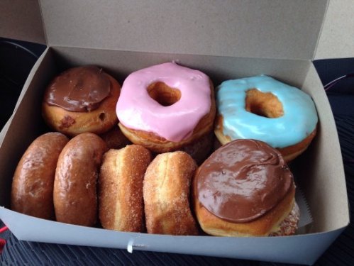 A box of assorted donuts, including chocolate, pink, and blue frosted varieties, along with glazed and cinnamon sugar donuts.