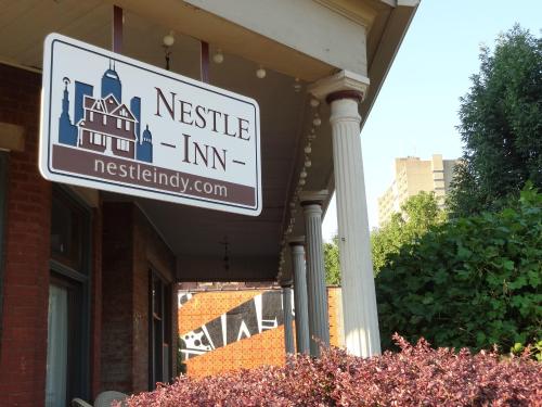 Sign for Nestle Inn, featuring a house graphic, hanging from a porch with greenery in the foreground.