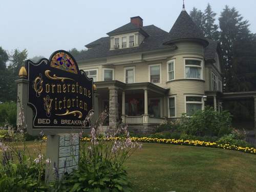 A large Victorian-style house with a sign reading "Cornerstone Victorian Bed & Breakfast" surrounded by flowers.