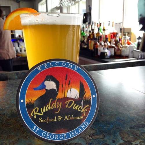 A glass of beer with an orange slice, next to a coaster for Ruddy Duck Seafood & Alehouse, St. George Island.