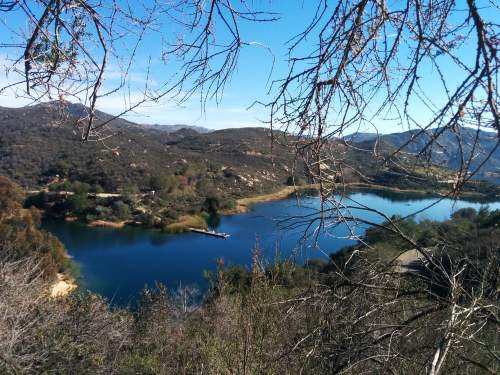 A serene lake surrounded by hills and trees under a clear blue sky.