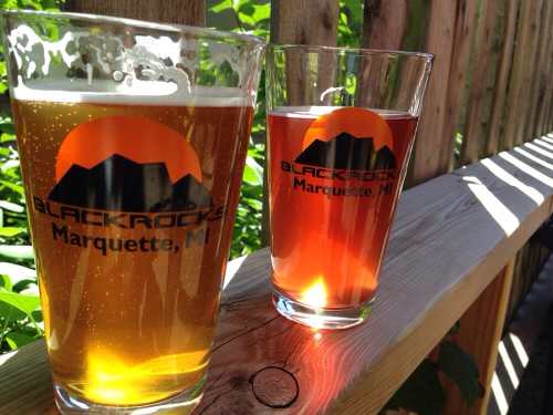 Two glasses of beer, one light and one dark, on a wooden surface with a logo for Blackrocks Brewery in Marquette, MI.