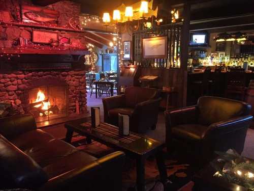 Cozy interior of a bar with a stone fireplace, leather chairs, and warm lighting, creating a welcoming atmosphere.