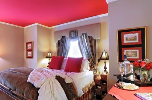 Cozy bedroom with a red ceiling, a neatly made bed, and romantic decor including roses and champagne.