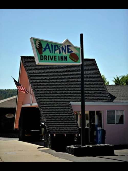 Sign for Alpine Drive Inn with an ice cream cone and burger icon, set against a clear blue sky.
