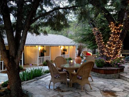 A cozy outdoor patio with a table and chairs, surrounded by trees and soft lighting, creating a warm ambiance.