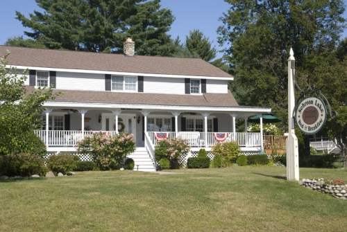 A charming two-story house with a porch, surrounded by greenery and a sign for "Sharon Lane Bed & Breakfast."