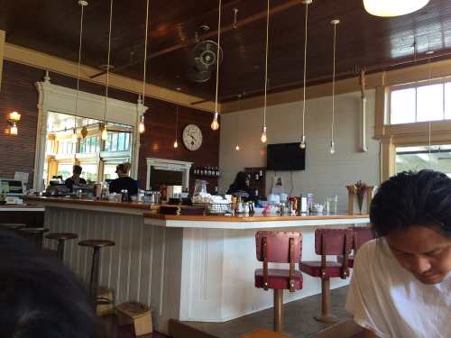 A cozy café interior with a wooden bar, hanging lights, and patrons enjoying their time.