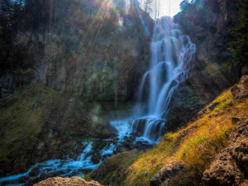 A stunning waterfall cascades down rocky cliffs, surrounded by lush greenery and illuminated by sunlight.