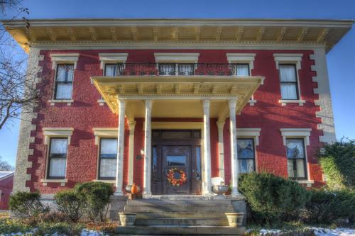 A large red brick house with white columns, a front porch, and a wreath on the door, surrounded by greenery.