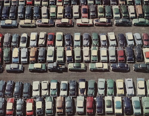 Aerial view of a crowded parking lot filled with various parked cars in different colors and models.