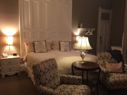 Cozy hotel room featuring a bed, two patterned chairs, a table, and soft lighting.