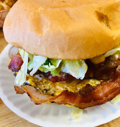 Close-up of a burger with bacon, lettuce, and cheese, served on a paper plate.