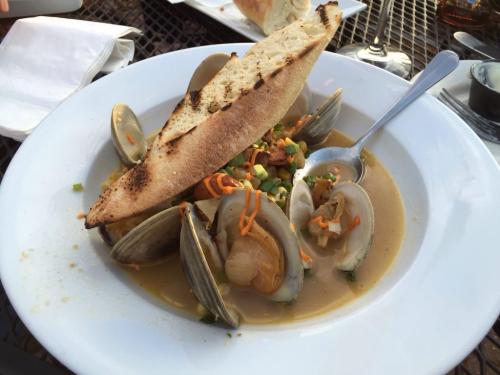A bowl of clam chowder topped with clams, vegetables, and a slice of toasted bread.