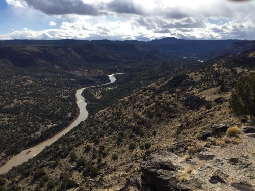 A winding river flows through a rugged landscape of hills and valleys under a cloudy sky.