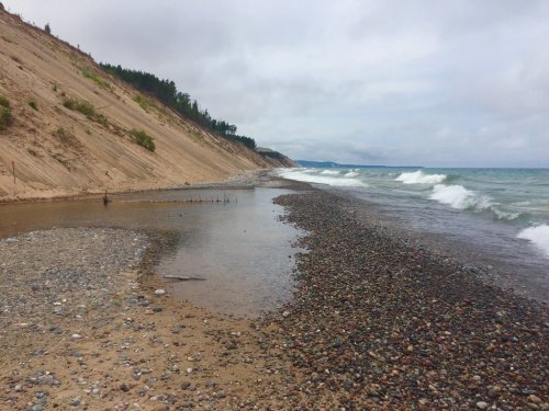 A rocky beach with gentle waves, surrounded by sandy cliffs and a cloudy sky.