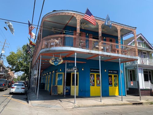 Colorful building with a wraparound balcony, flags, and a sign reading "Paw Paw's" in a lively street setting.