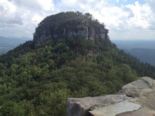 A rocky mountain peak surrounded by lush green trees under a cloudy sky.