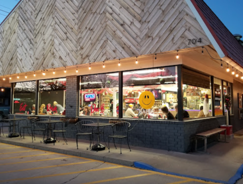A cozy restaurant with large windows, string lights, and diners enjoying their meals inside and outside.
